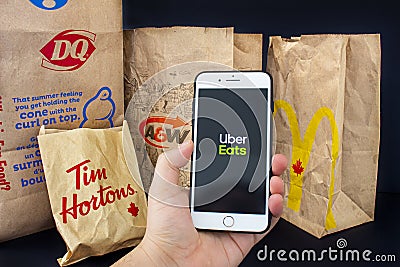 A person holding an iPhone Plus with the Uber Eats application open with delivered food Editorial Stock Photo