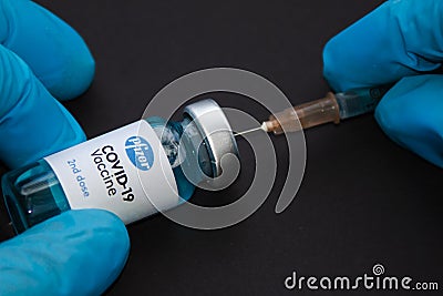 A health worker wearing gloves with a Pfizer Covid-19 vaccine vial and a syringe on a black Editorial Stock Photo