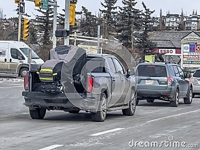 A Sierra 1500 pickup truck transporting a covered snowmobile during the winter Editorial Stock Photo