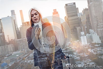 Calling to partner. Beautiful business woman in suit carrying her luggage and looking at smartphone while going to Stock Photo