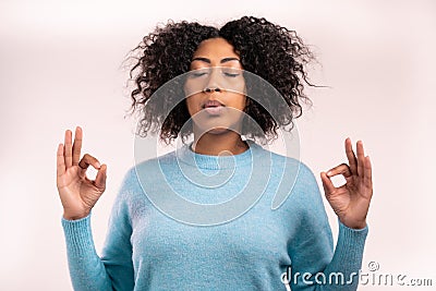 Calm african woman in blue relaxing, meditating. She calms down, breathes deeply with mudra om on white studio Stock Photo