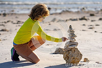 Calm child play with pyramid stones balance on the sand of summer beach. Child play with stack of stones. Child play on Stock Photo