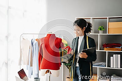 Calm curly brunette dark skinned woman on desk in office of fashion designer and holds tablet and smartphone Stock Photo
