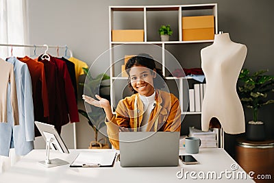 Calm curly brunette dark skinned woman on desk in office of fashion designer and holds tablet and smartphone Stock Photo