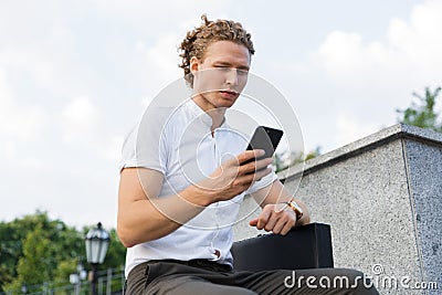 Calm curly business man with briefcase using smartphone Stock Photo