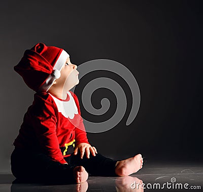 Calm infant boy toddler in santa claus costume is sitting barefooted on ice looking up carefully in corner at copy space Stock Photo