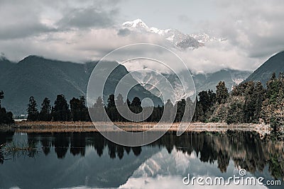 calm and lonely landscape of snowy mountains covered by clouds stunning stormy day at calm water lake amid nature Stock Photo