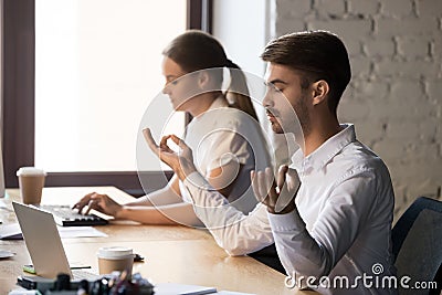 Calm male employee sit near computer meditating at workplace Stock Photo
