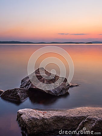 Calm and meditation concept. Sunset on the lake, rocks in the foreground, quiet water, cloudless sky Stock Photo