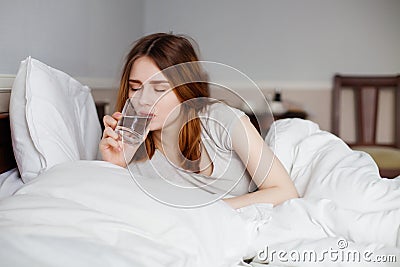 Calm pretty woman drinking a glass water in bright bedroom