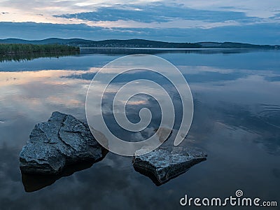 Calm, serenity, meditation concept. Sunset on the lake, stones in the water in the foreground, quiet water, cloudless sky Stock Photo