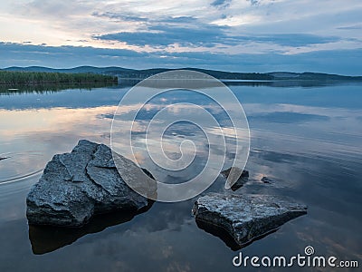 Calm, serenity, meditation concept. Sunset on the lake, stones in the water in the foreground, quiet water, cloudless sky Stock Photo