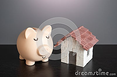 Calm sleepy pig piggy bank with a house. Collect money to buy a house. Deposits and real estate investments Stock Photo