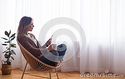 Calm woman networking on smartphone, sitting with cocoa Stock Photo