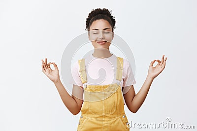 Calming down and getting rid of stress inside. Calm and cute good-looking dark-skinned female in yellow trendy overalls Stock Photo