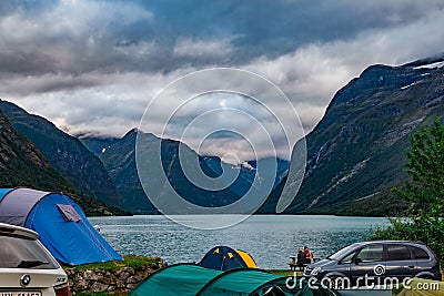 Calming view on camping people by the fjord shore against mountains and dramatic clouded sky Editorial Stock Photo