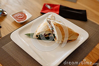 Calzone pizza halves on bamboo sheet in square plate on wooden table Stock Photo