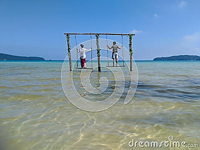 Cambodian Asian Man & Woman Standing on Swings in the Ocean Editorial Stock Photo