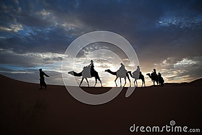 Camel train silhouetted against colorful sky crossing the Sahara Stock Photo