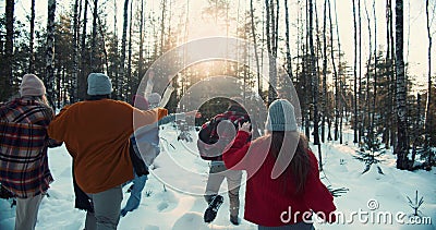 Camera follows group of excited happy friends run through snowy winter forest on sunny Christmas vacation slow motion. Stock Photo