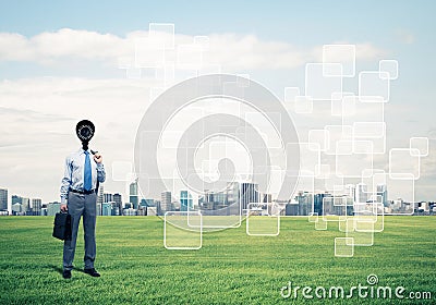 Camera headed man standing on green grass against modern citysca Stock Photo