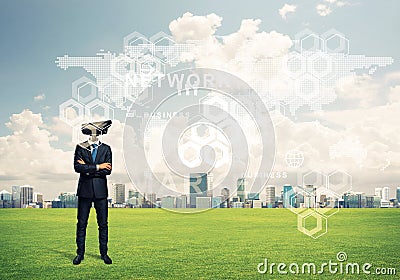 Camera headed man standing on green grass against modern cityscape Stock Photo