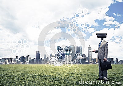 Camera headed man standing on green grass against modern cityscape Stock Photo