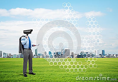 Camera headed man standing on green grass against modern cityscape Stock Photo