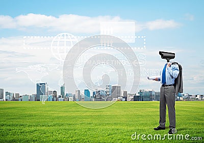 Camera headed man standing on green grass against modern cityscape Stock Photo