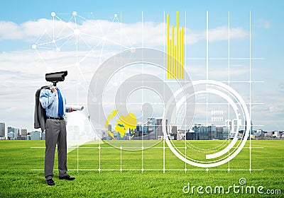 Camera headed man standing on green grass against modern cityscape Stock Photo