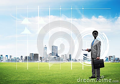 Camera headed man standing on green grass against modern cityscape Stock Photo