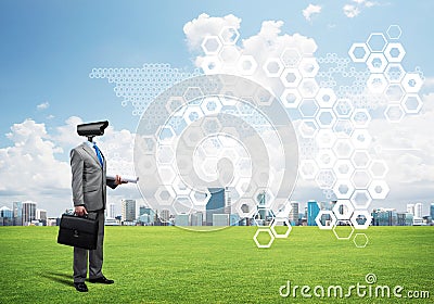 Camera headed man standing on green grass against modern cityscape Stock Photo