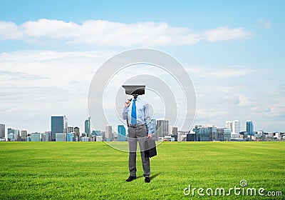 Camera headed man standing on green grass against modern cityscape Stock Photo