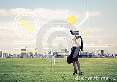 Camera headed woman standing on green grass against modern cityscape Stock Photo