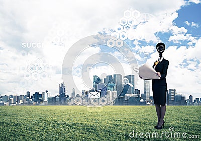 Camera headed woman standing on green grass against modern cityscape Stock Photo