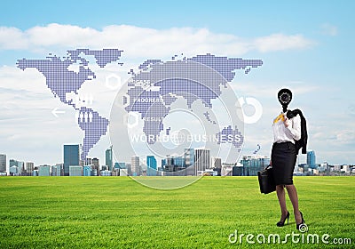 Camera headed woman standing on green grass against modern cityscape Stock Photo