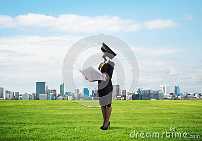 Camera headed woman standing on green grass against modern cityscape Stock Photo