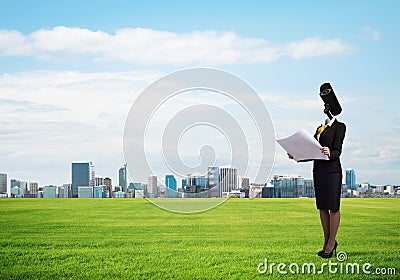 Camera headed woman standing on green grass against modern cityscape Stock Photo