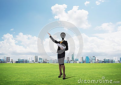 Camera headed woman standing on green grass against modern cityscape Stock Photo