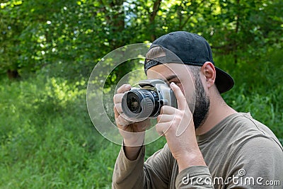 The camera smokes in the hands of photographer takes a photo in nature. young bearded man photographs outdoors Stock Photo