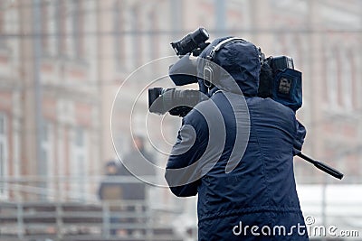 The cameraman shoots a television report in the rain on the street Stock Photo