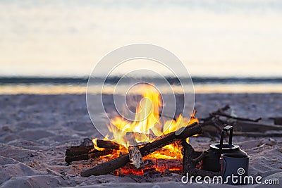 Campfire burns on the seashore next to waves during sunset Stock Photo