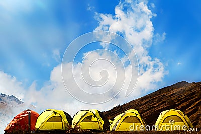 Campground in the mountains. Many yellow adn red tents against the blue sky with amazing clouds Stock Photo