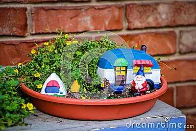Camping gnome fairy garden in planter with minature camper and tent against blurred brick wall Stock Photo