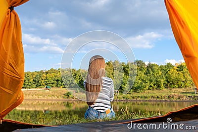 Camping on lake shore at sunset, view from inside tourist tent. Girl enjoy nature in front of tent Stock Photo