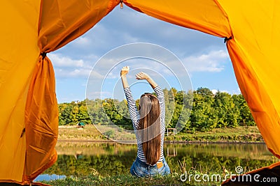 Camping on lake shore at sunset, view from inside tourist tent. Girl enjoy nature in front of tent Stock Photo