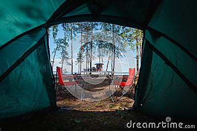 Camping in the middle of the forest, taken from inside the tent. View of the folding table and chairs with gas stove in the backgr Stock Photo