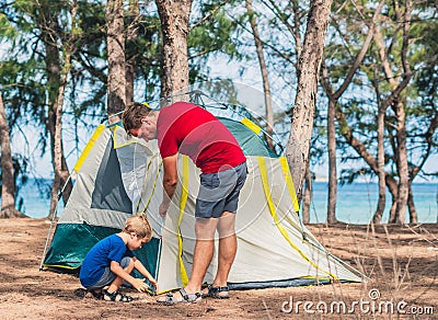 Camping people outdoor lifestyle tourists put up set up green grey camp site summer forest near lazur sea. Boy son helps Stock Photo