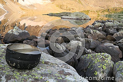 Camping pot with water in the background of mountains mirror reflection in the lake. Hiking motivational image Stock Photo