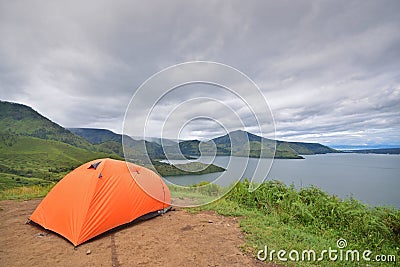 Camping in professional outdoor orange colour tent at the top of a hill overlooking dramatic lake view and cloud Stock Photo